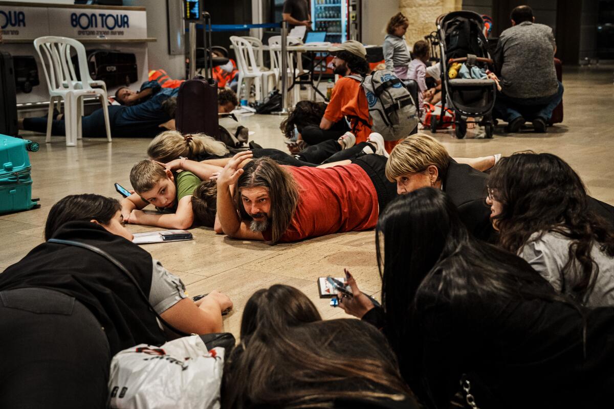 Люди лежат на земле во время сирен воздушной тревоги в аэропорту Бен-Гурион недалеко от Тель-Авива.