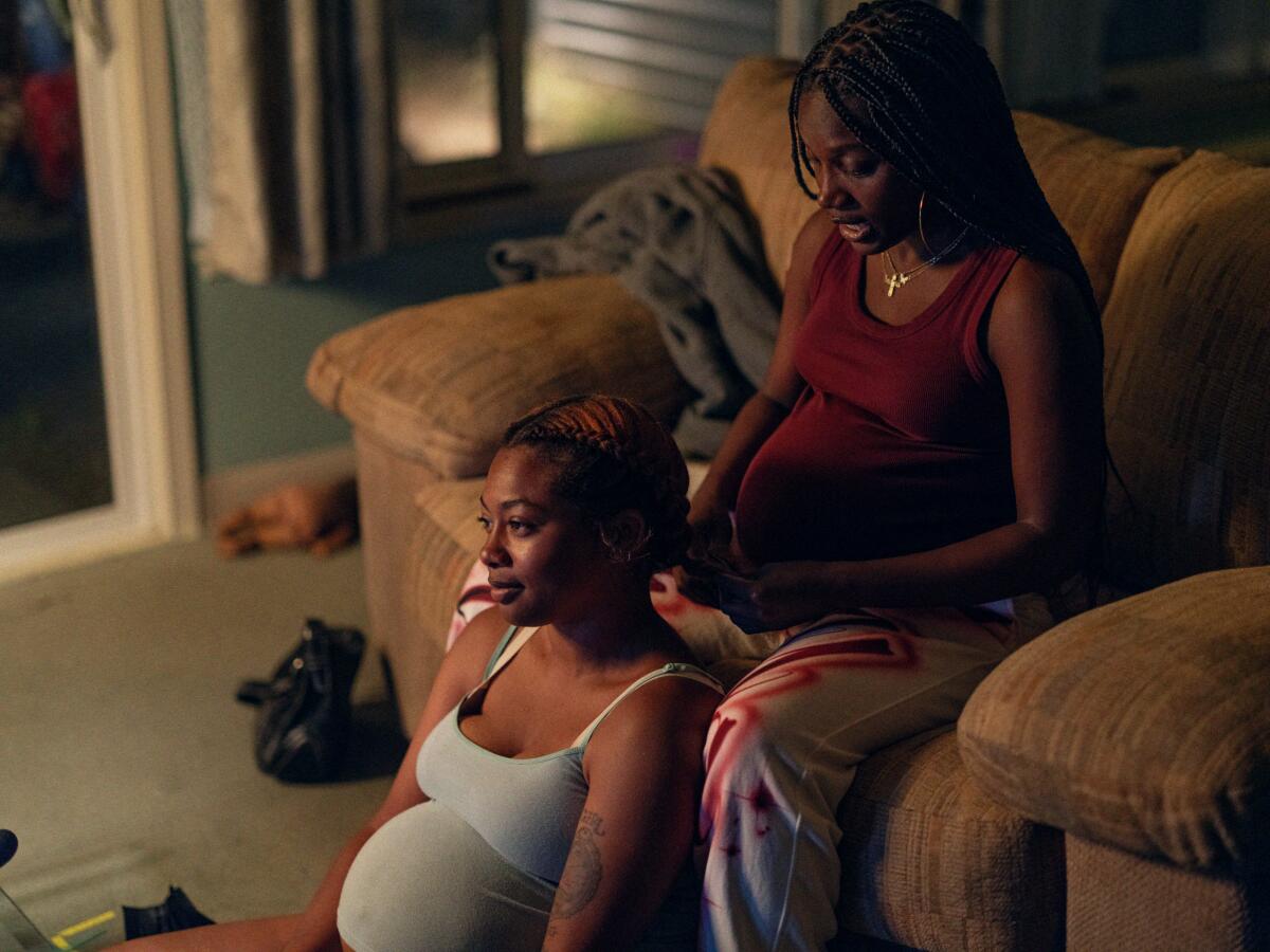 A pregnant woman gets a shoulder massage from a pregnant friend in her living room.
