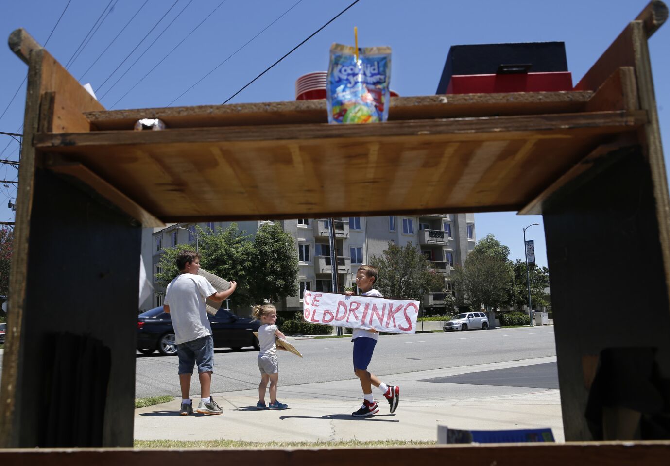 From left, Aaron Stevens, 11, Alida Stevens, 4, and Brian Botts, 9, wave down customers as they sale refreshments on a hot summer day in Van Nuys. "We want to help people hydrate while helping ourselves," Aaron Stevens said.