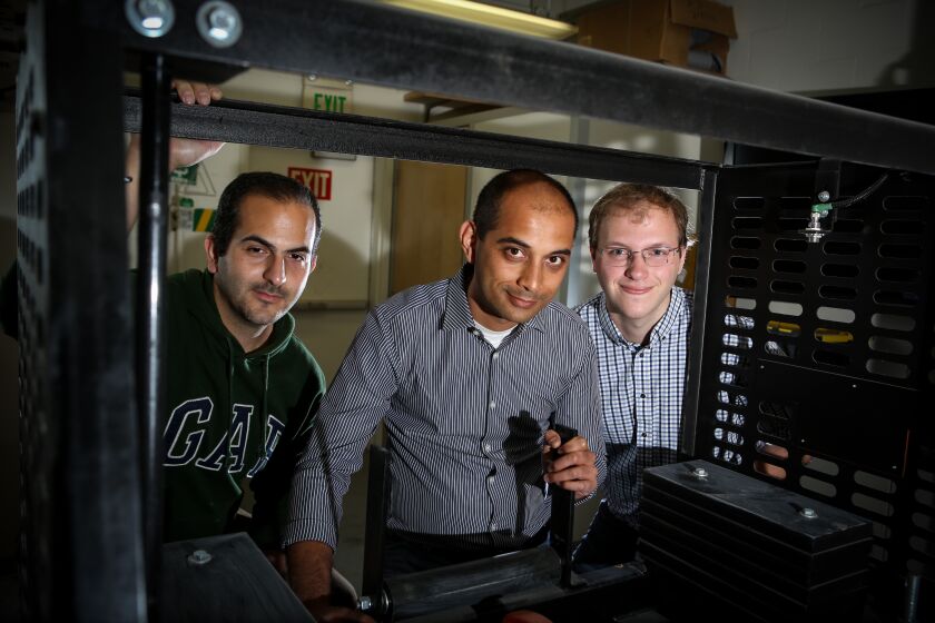 Los Angeles, CA., December 2, 2019: Team leader Gaurav Sant (center), Associate Professor and Henry Samueli Fellow of Civil and Environmental Engineering at UCLA, along with Iman Mehdipour (left), post-doctoral scholar, and Gabe Falzone (right), post-doctoral scholar, stand in one of their laboratories behind a machine that forms bricks on Monday, December 2, 2019 at UCLA. Sant, Mehdipour, and Falzone lead a team at UCLA going after a $10-million prize that will go to whoever comes up with the best way to turn carbon pollution into something valuable. Their plan is to capture carbon from a coal-fired power plant and turn it into concrete bricks. (Jason Armond / Los Angeles Times)
