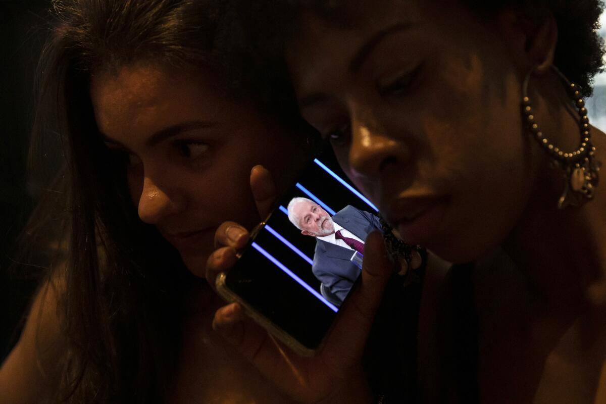 Women listen on a mobile phone to an interview of former president Luiz Inacio Lula da Silva.