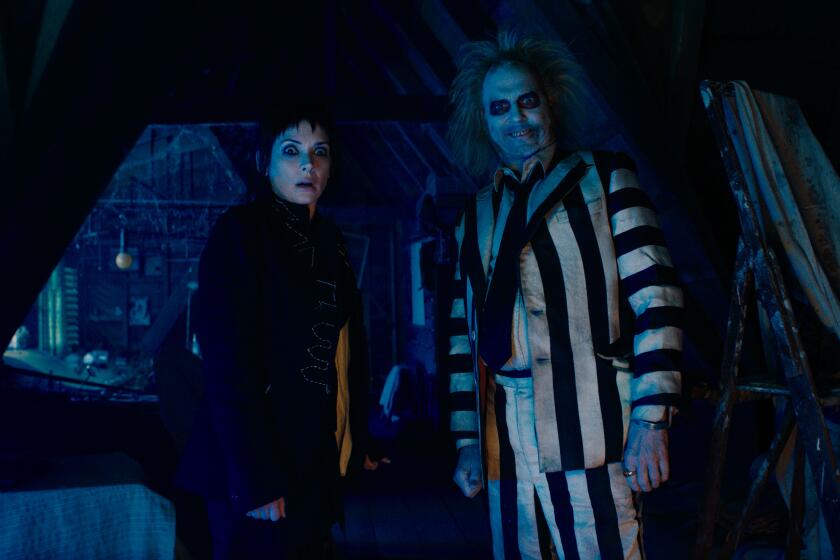 A woman in black poses with a demon in a striped shirt.