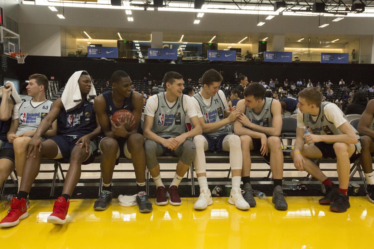 Players from around the world, including Charles Bassey in red shoes and N'Faly Dante holding the ball, joke around with fellow players during the fourth annual Basketball Without Borders global camp in El Segundo.