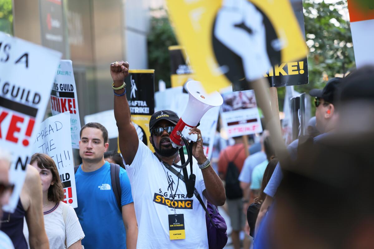 A man holding a bullhorn raises a fisted hand as he stands near people holding signs 