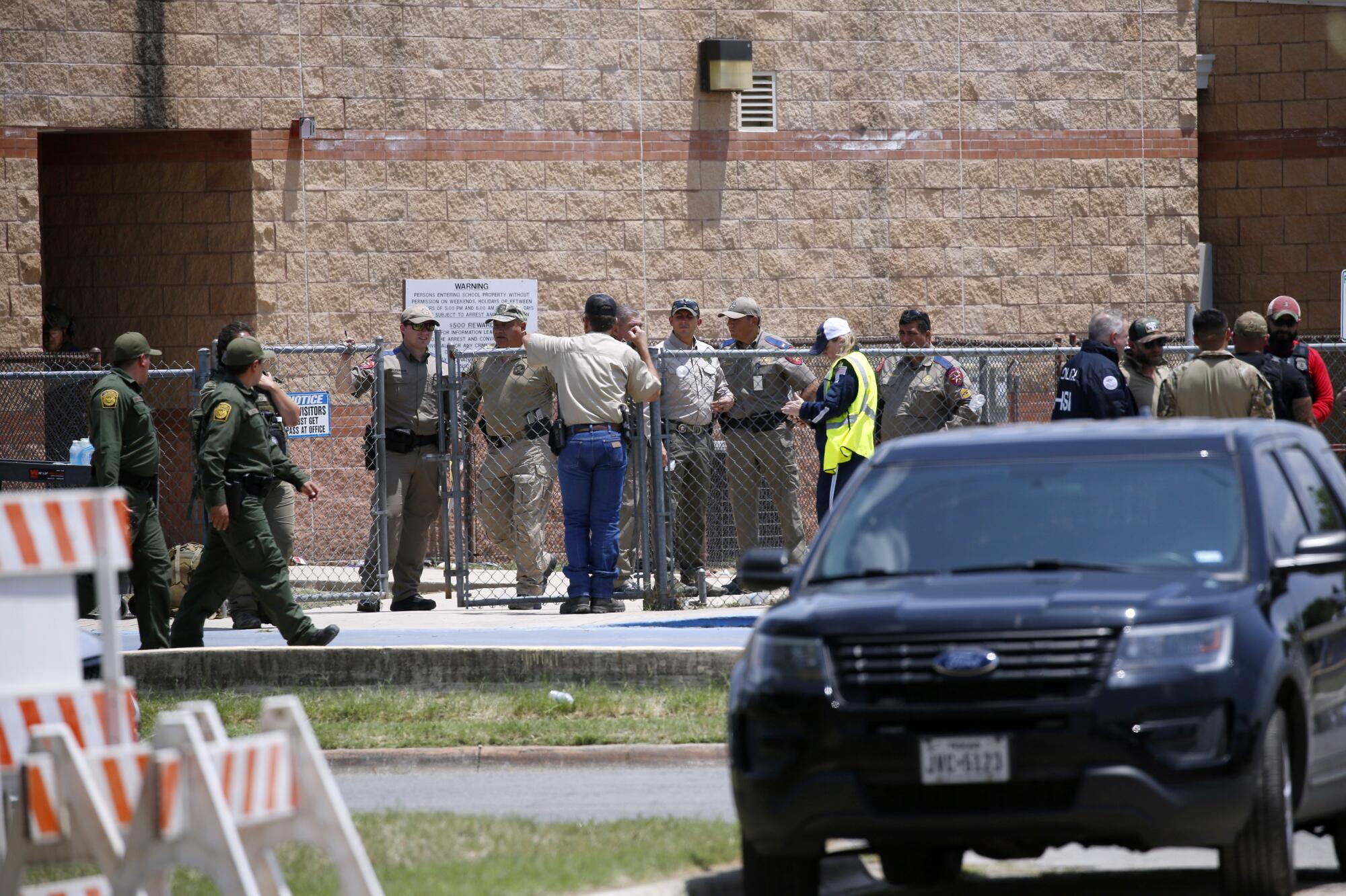 People in uniform stand along a wire fence in front of a brick building 