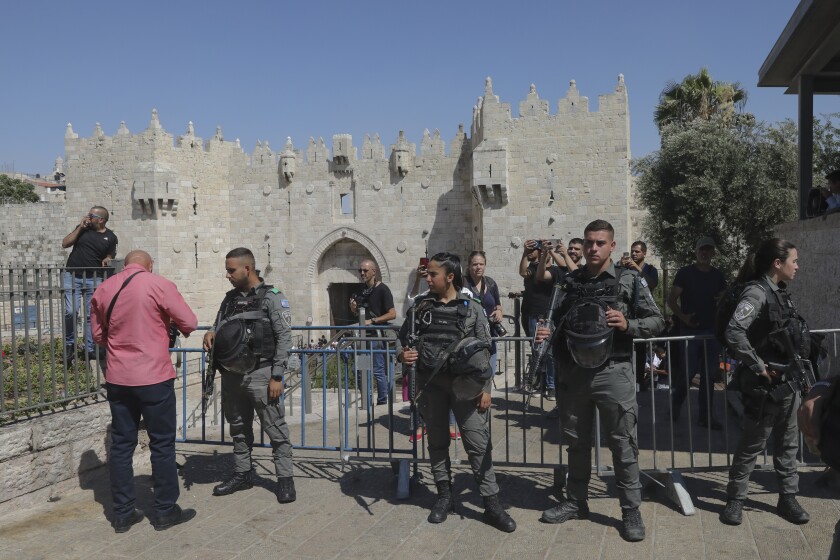 Uniformed and armed officers stand in front of barricades near a fortress-like stone wall 