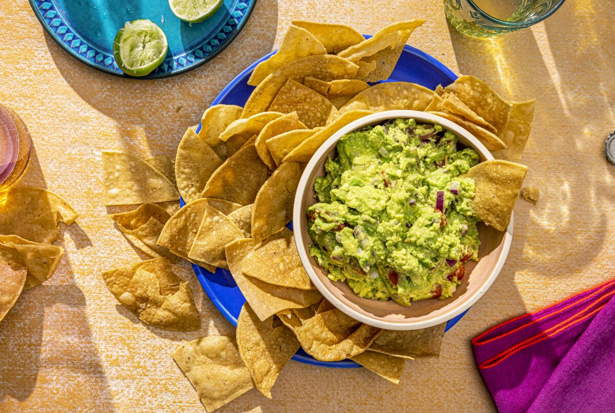 A hand dips a chip into a bowl of guacamole 