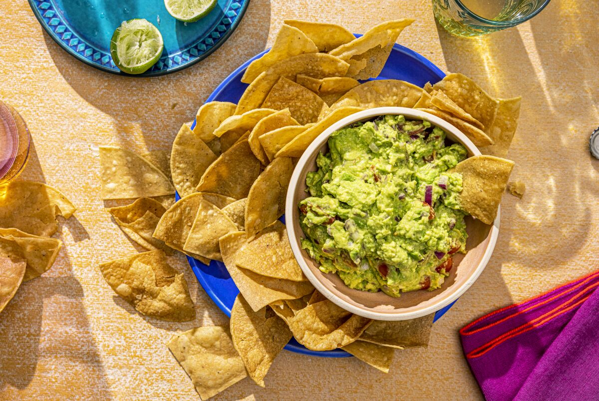 A hand dips a chip into a bowl of guacamole