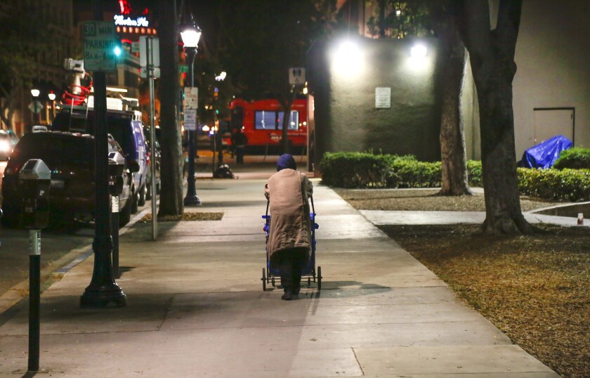 A homeless woman pushes her belongings in a cart as she walks along Third Avenue in downtown San Diego.
