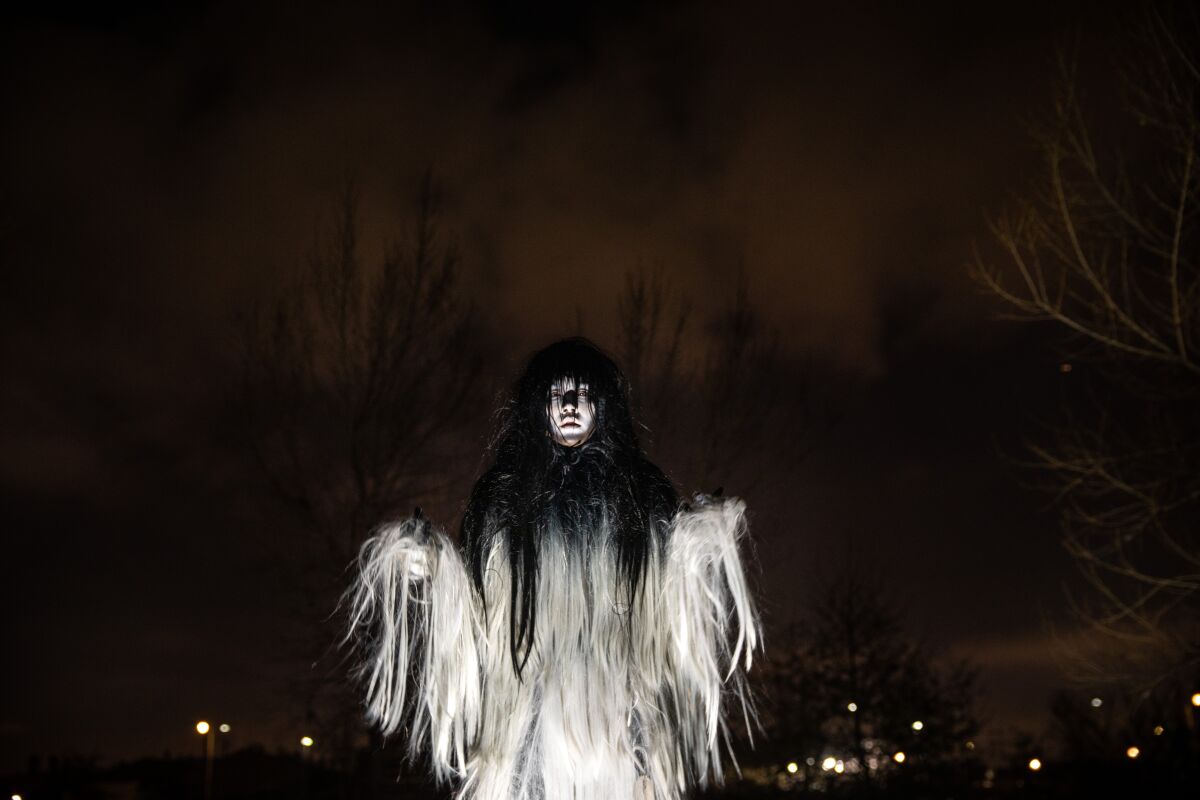 An actor in a ghostly ensemble made of black and white hair performs against a dark sky in "Sweet Land" 