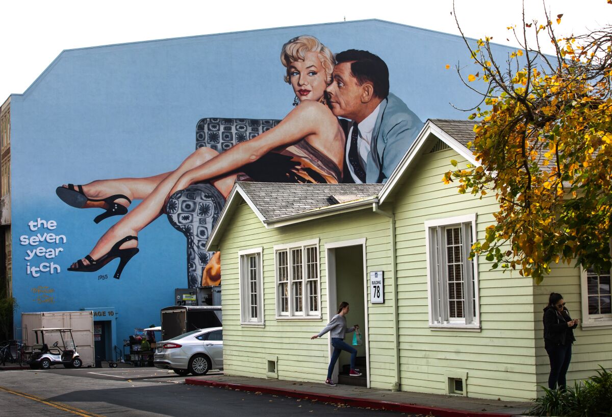 A mural of a woman and a man on a tall building appears above a bungalow.
