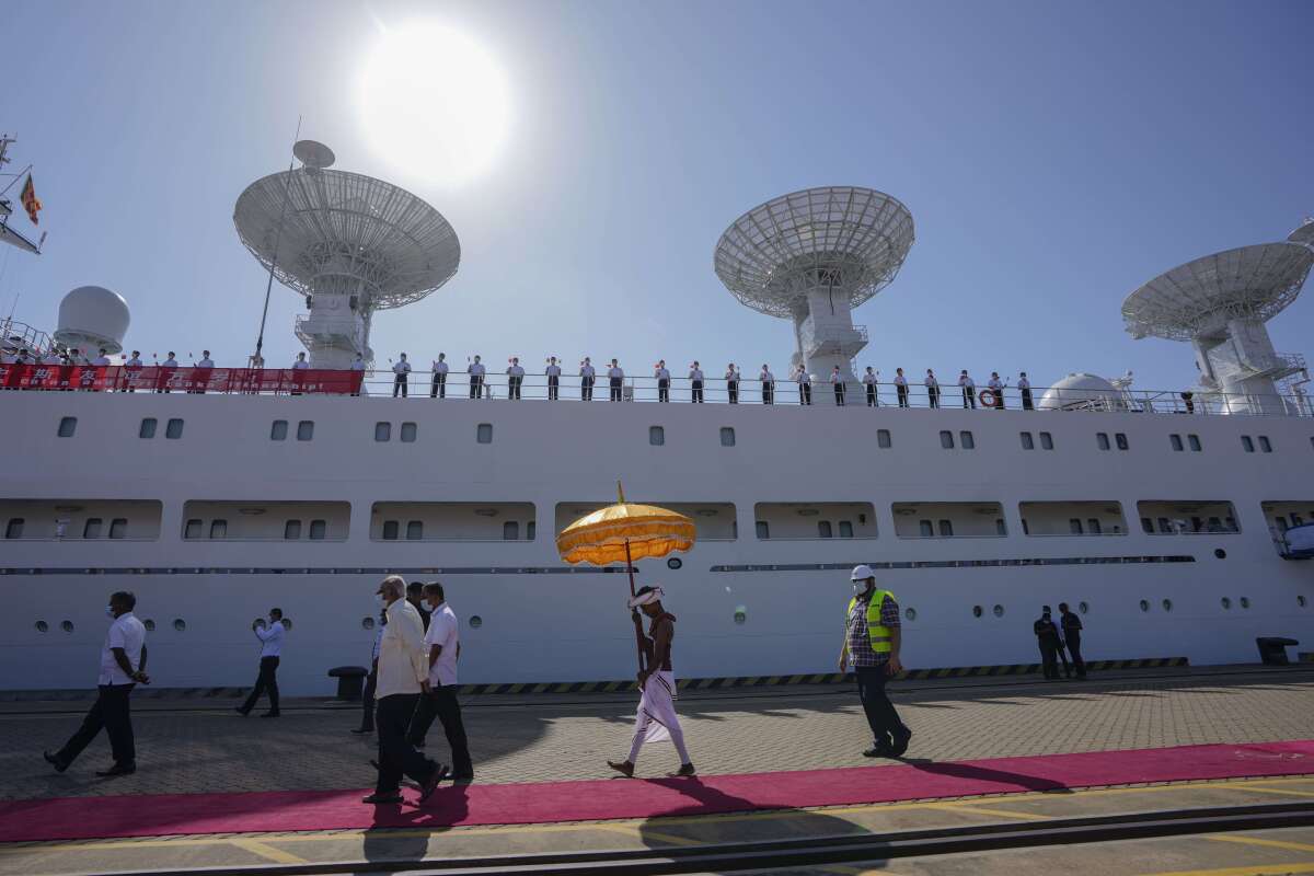 A Sri Lankan traditional dancer carries a decorative umbrella as the crew of Chinese scientific research ship Yuan Wang 5 wave Chinese flags after arriving at Hambantota International Port in Hambantota, Sri Lanka, Tuesday, Aug. 16, 2022. The ship was originally set to arrive Aug. 11 but the port call was deferred due to apparent security concerns raised by India. (AP Photo/Eranga Jayawardena)