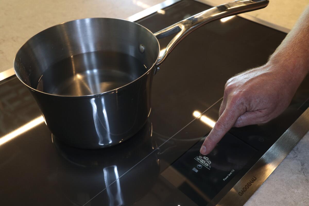 A person presses a button on an induction cooktop with a pot of water on it