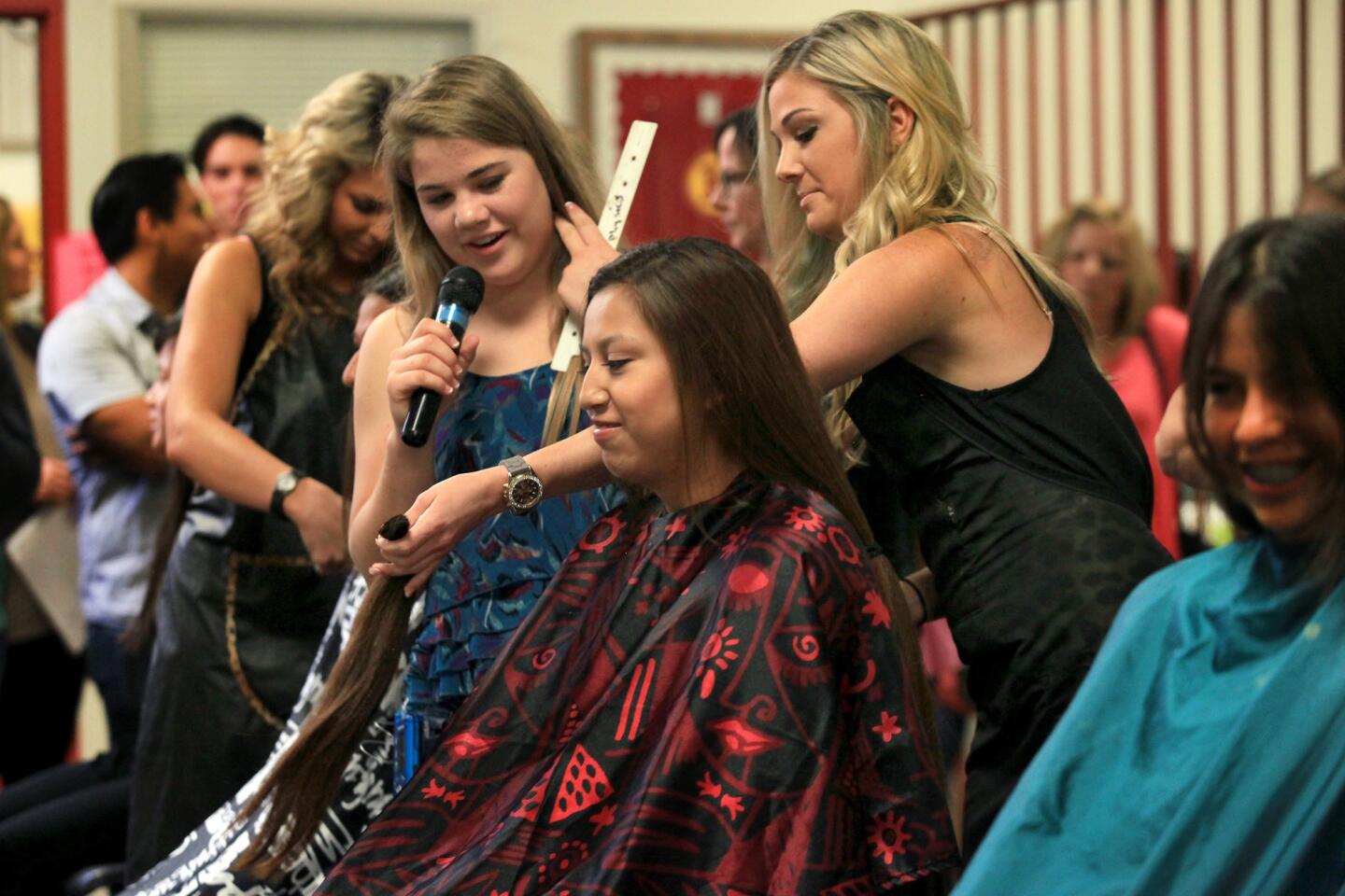 Morgan Miller, center left, Estancia High School ASB commissioner of community involvement, announces Tuesday that junior Maggie Aguilar, center, had hairstylist Caitlin Doty, center right, cut off 16 inches of her hair to donate to nonprofit Children With Hair Loss.
