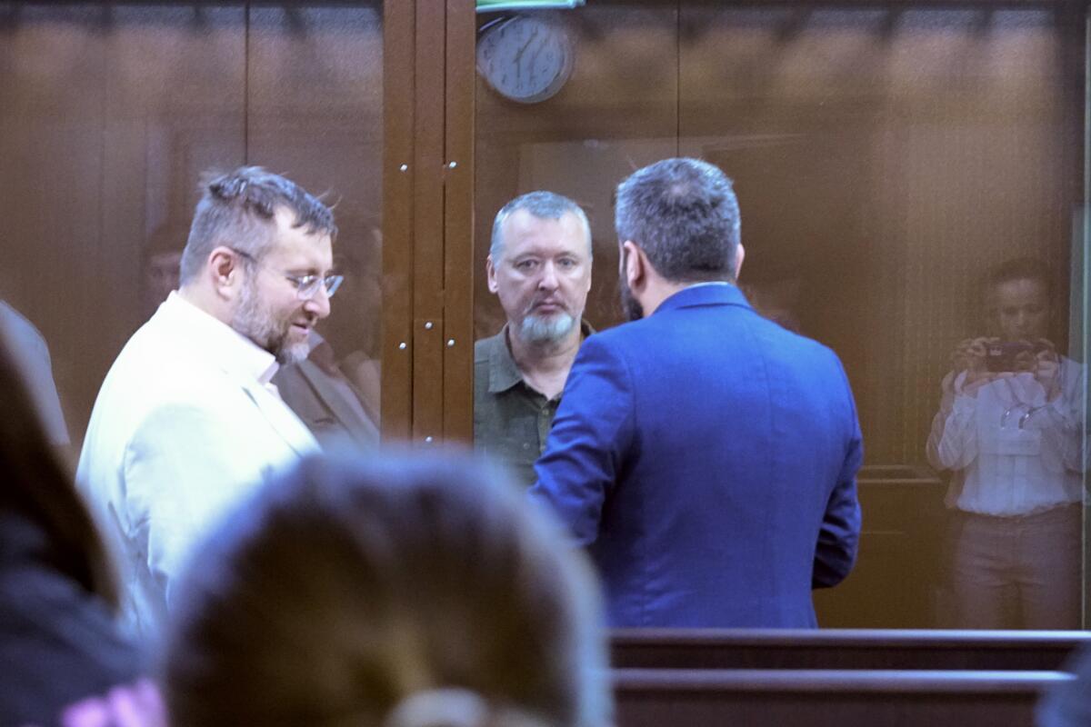 Igor Girkin speaks with his lawyer standing in a glass cage in a courtroom.
