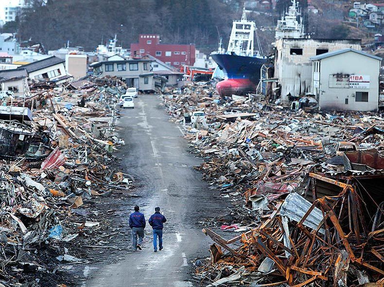 Government officials walk down a recently cleared roadway where the earthquake-spawned tsunami caused a massive fuel spill and fire on March 17.