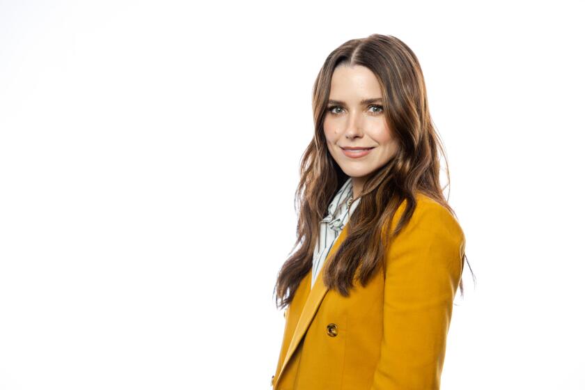Sophia Bush wears a yellow blazer and smiles against a white background