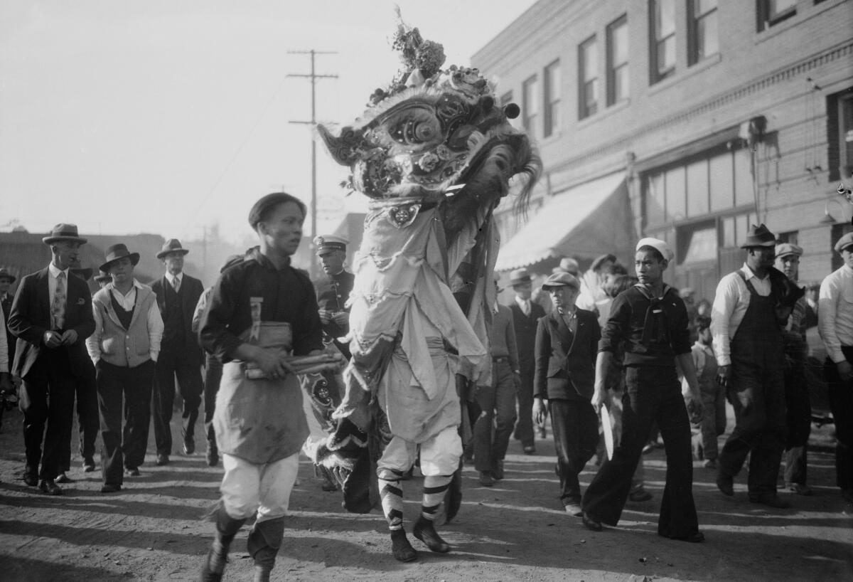 People walk in a city street alongside a person in an elaborate lion costume.