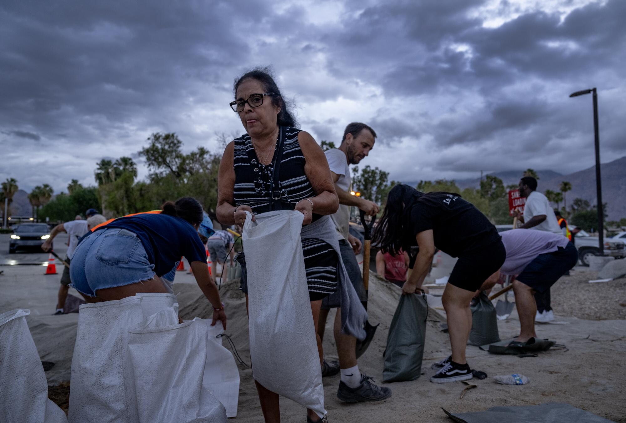 With storm clouds looming overhead, Bernadette Duran of San Gabriel carries sandbags to protect her vacation home.