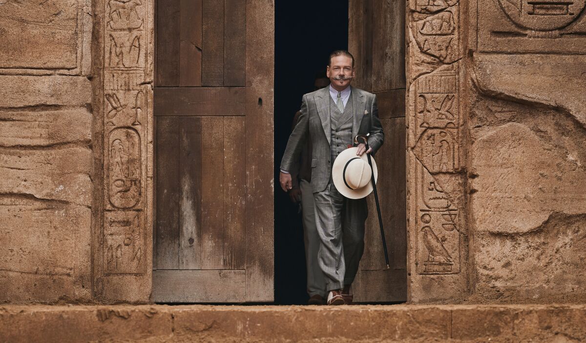 Kenneth Branagh walks outside with hat and cane in hand in a scene from "Death on the Nile."