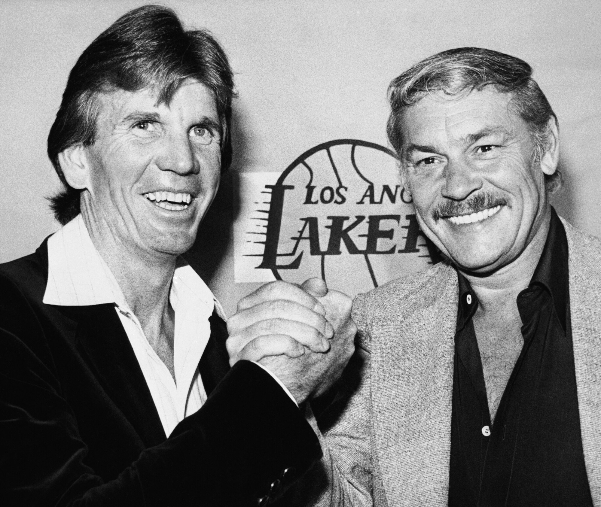 Two men clasp hands in front of a Lakers logo