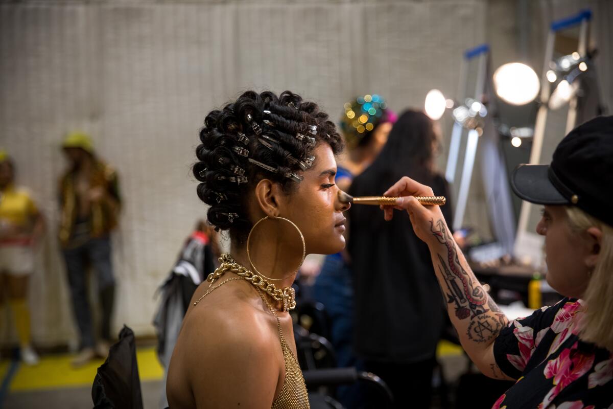 A makeup artist brushes makeup onto a performer's face  behind the scenes of a TV production.