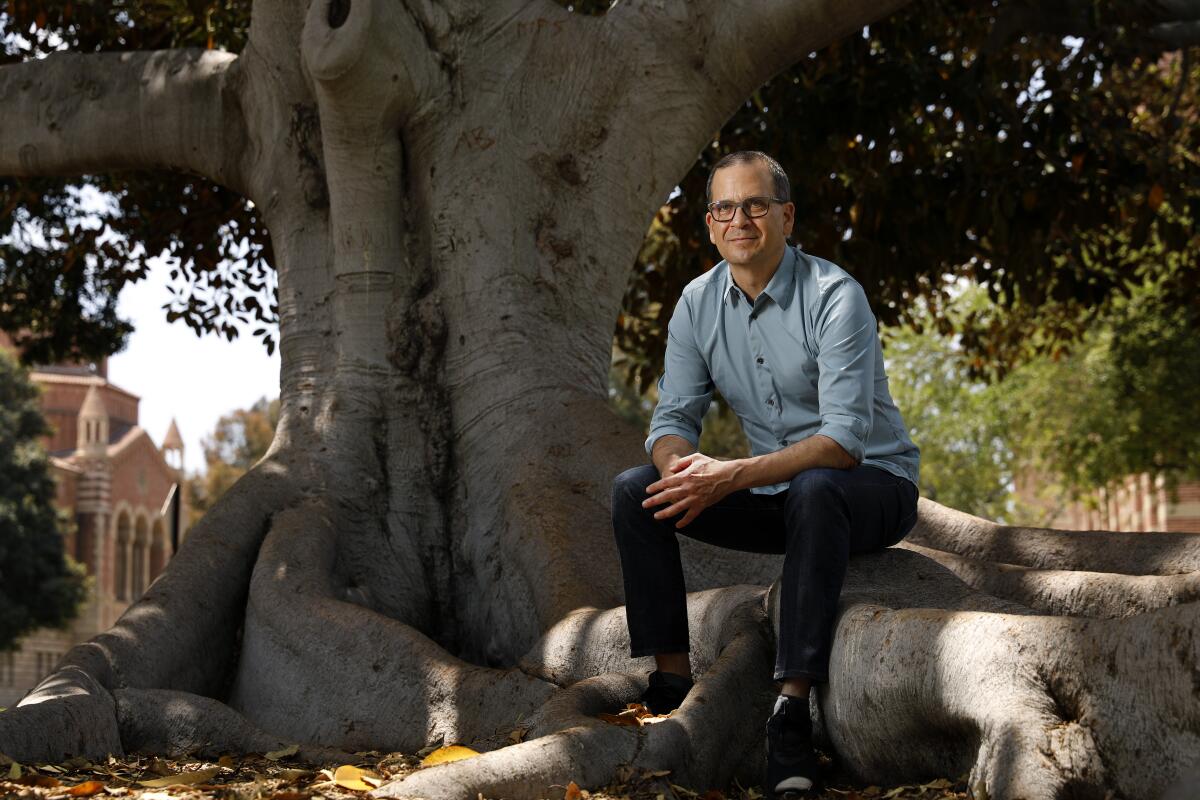 Chon Noriega sits on a tree stump; views of one of UCLA's Romanesque buildings can be see in the distance