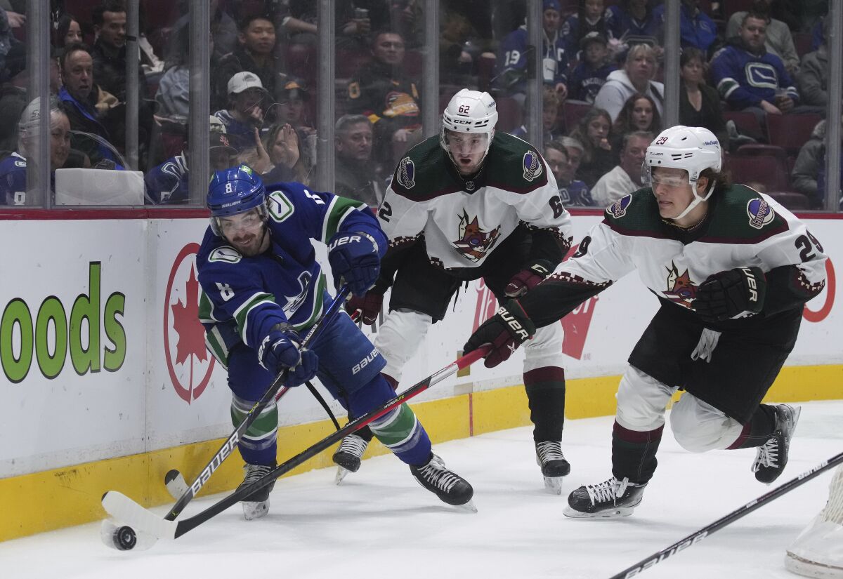 Vancouver Canucks' Conor Garland (8) vies for the puck against Arizona Coyotes' Barrett Hayton (29) as Janis Moser (62) watches during the first period of an NHL hockey game Thursday, April 14, 2022, in Vancouver, British Columbia. (Darryl Dyck/The Canadian Press via AP)
