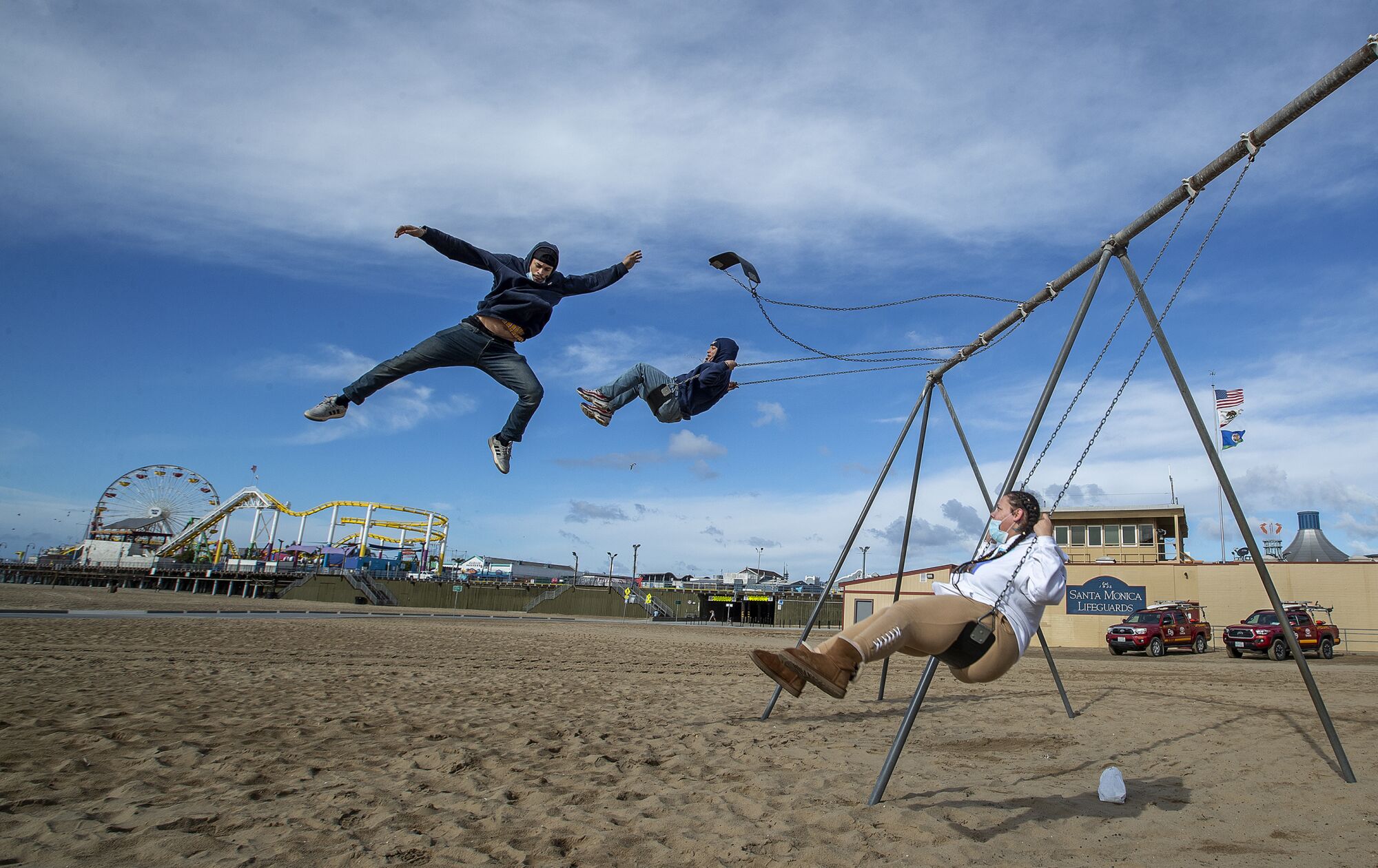 Three people use the swings on a beach