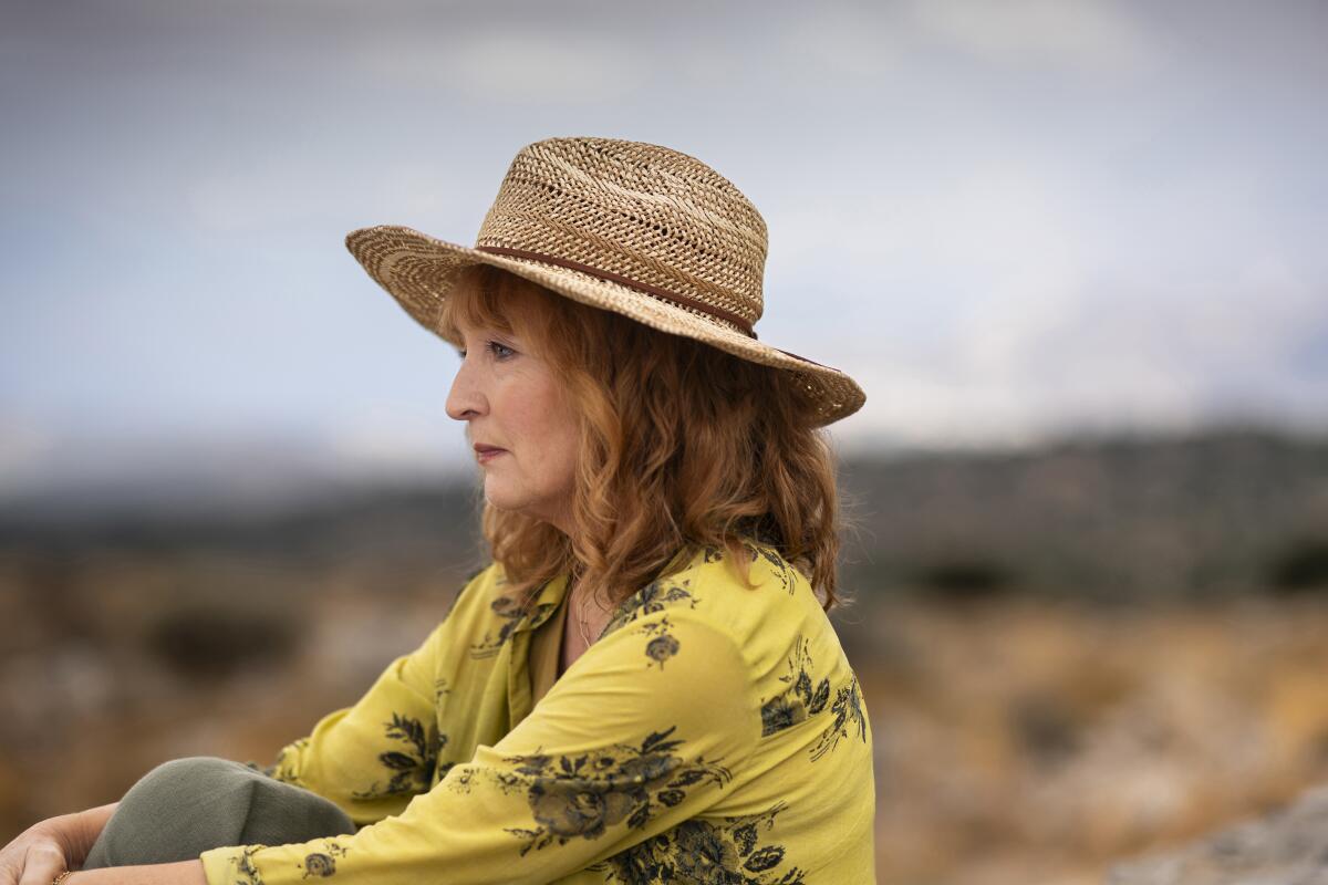 A woman in a straw hat and yellow blouse sits on a beach.