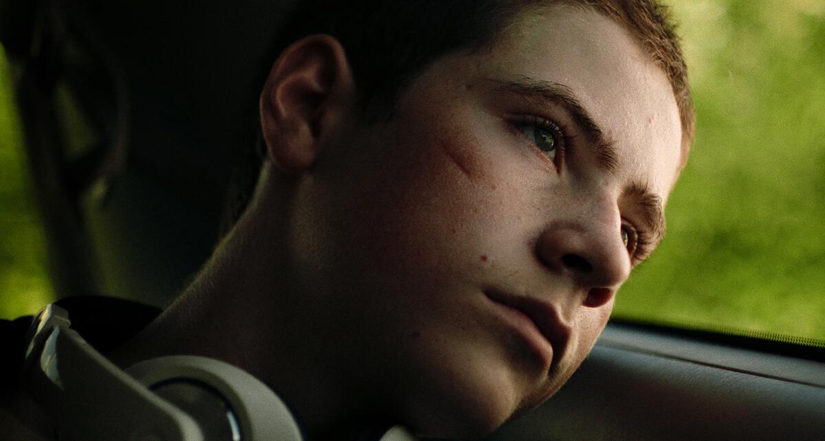 A serious-looking teen boy leans his head against the window while riding in a bus in "Invincible."