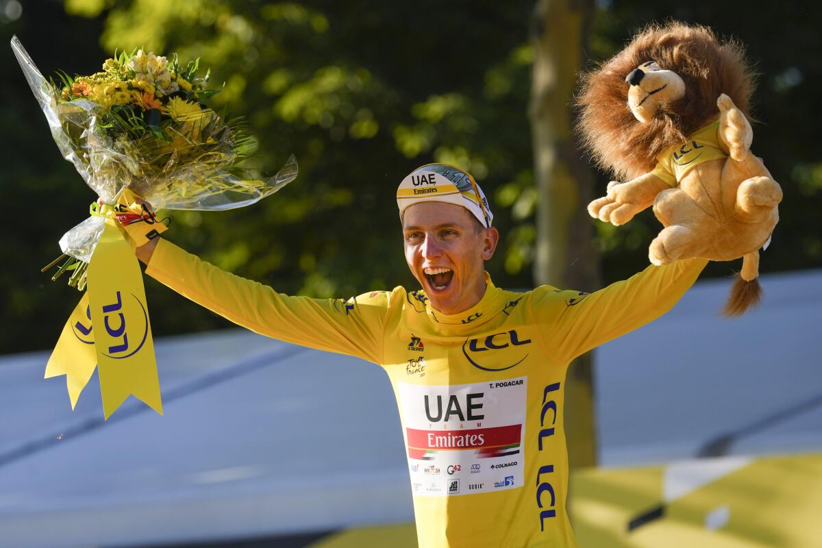 Tour de France winner Tadej Pogacar celebrates by holding up a stuffed lion toy and a flower bouquet.
