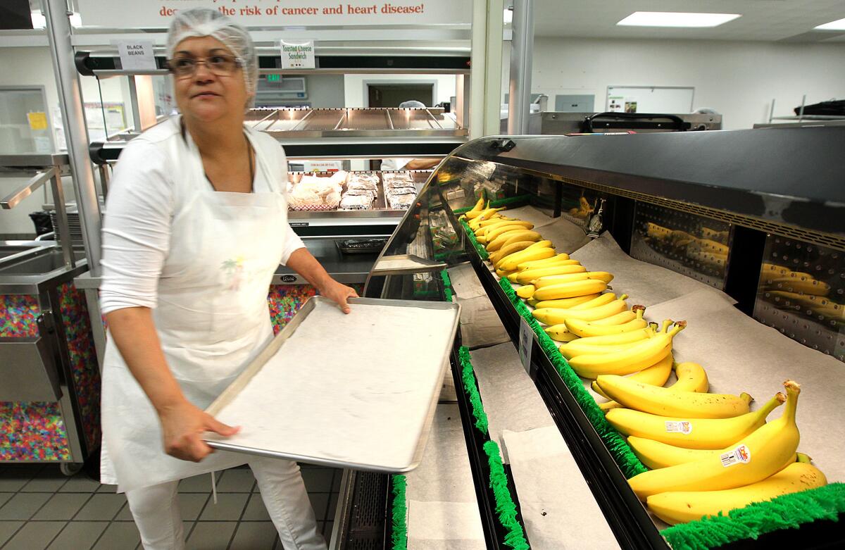 Kitchen worker Linda Gomez stocks bananas in a display case inside the cafeteria during lunch time at Bravo Medical Magnet High School in Los Angeles
