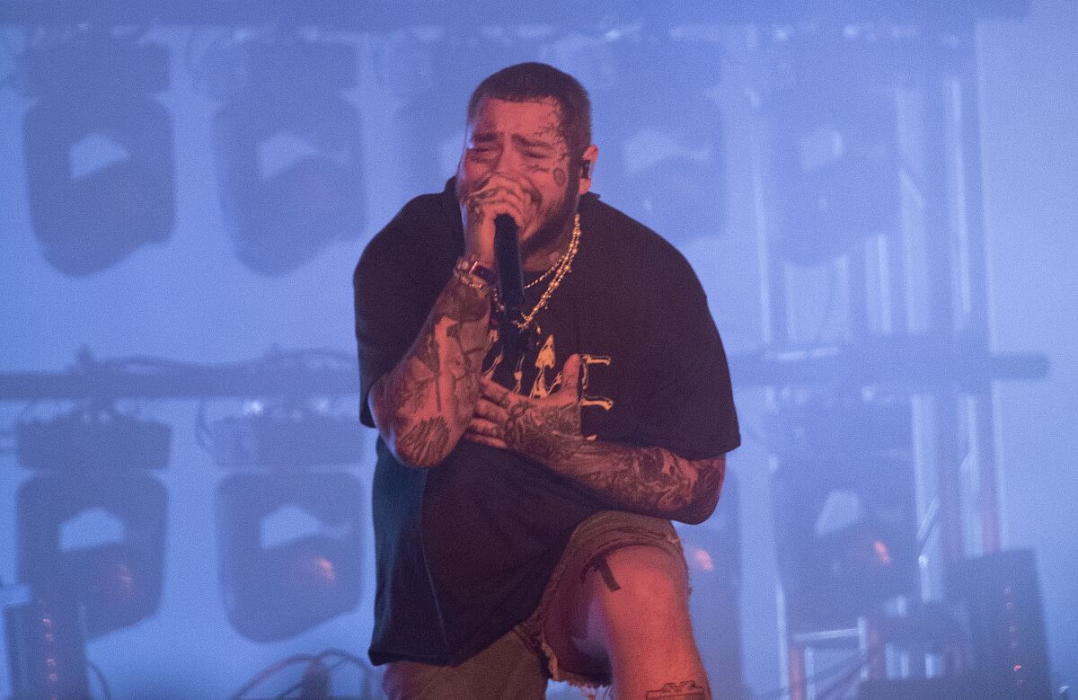 A man with tattoos on his arms and face sings onstage.