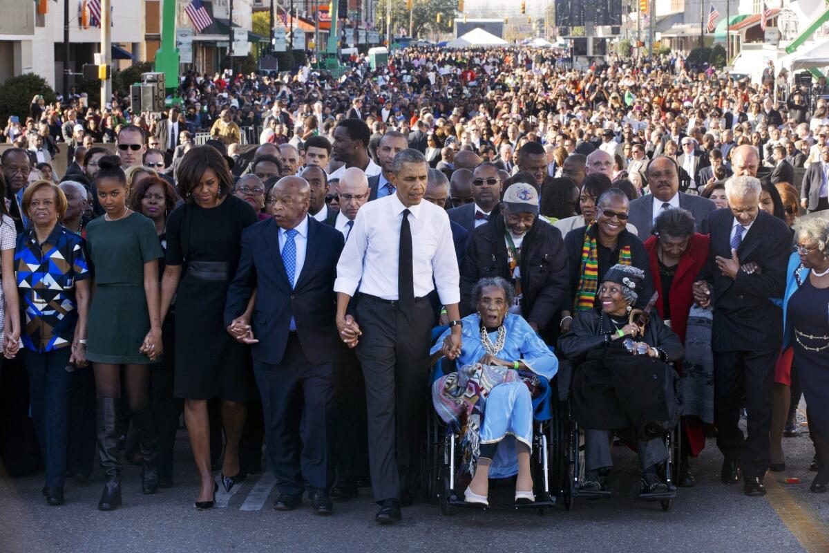 President Barack Obama walks as he holds hands with Amelia Boynton Robinson, who was beaten during "Bloody Sunday," as they, the first family and others walk across the Edmund Pettus Bridge in Selma, Ala.