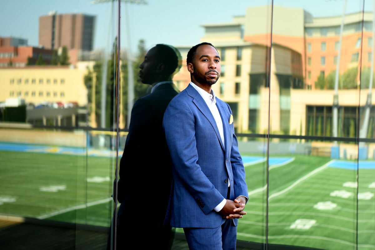 UCLA athletic director Martin Jarmond stands in front of a reflection of a field.