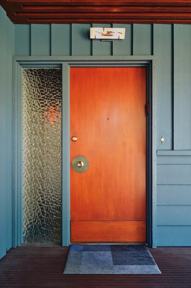 An orange door with a privacy-glass sidelight on a blue house.