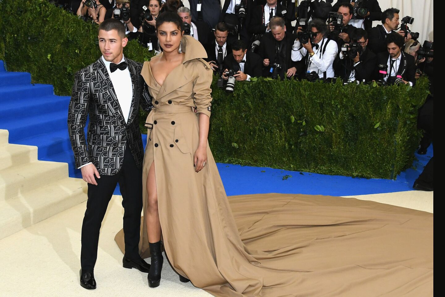 Nick Jonas in a black and white Art Deco jacquard tuxedo jacket and black tuxedo pants from Ralph Lauren Purple Label, with Priyanka Chopra in a Ralph Lauren Collection cstom trench coat evening Gown on the red carpet at the 2017 Met Gala.
