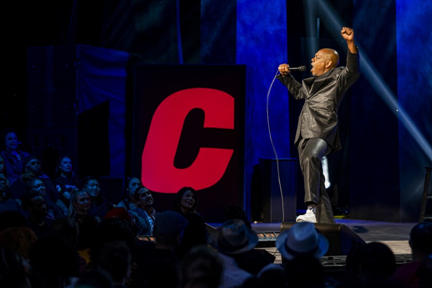 A man on stage raises his fist next to a giant red "C"