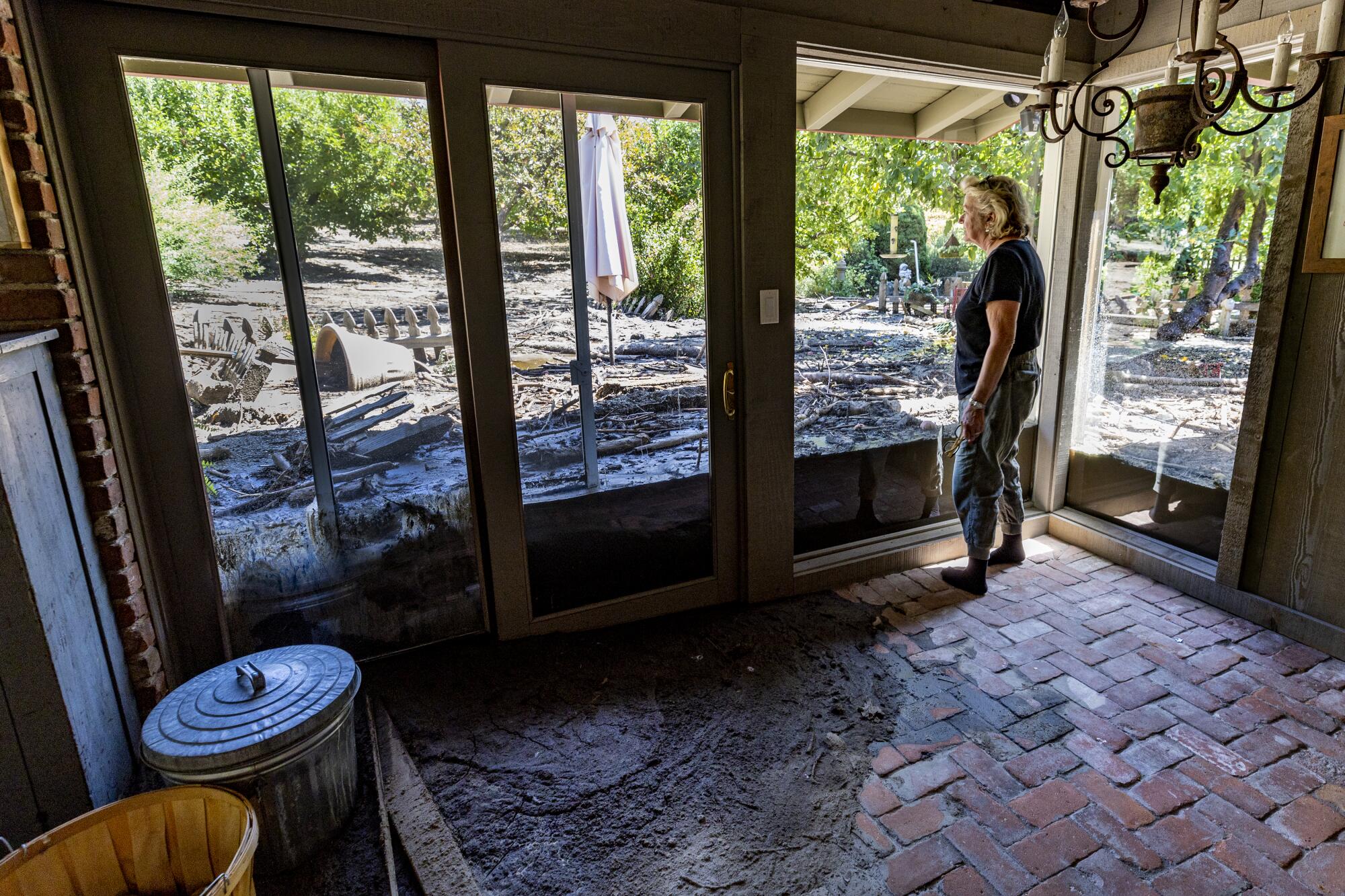 A woman looks out into her yard covered in a layer of mud from a recent mudslide.
