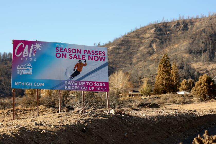 Wrightwood, CA - October 09: A sign showcasing a season pass for skiing is displayed surrounded by burnt branches and trees from the after effects of the bridge fire on Wednesday, Oct. 9, 2024 in Wrightwood, CA. The Bridge Fire that erupted in the Angeles National Forest has destroyed more than 30 homes and scorched more than 50,000 acres. (Michael Blackshire / Los Angeles Times)