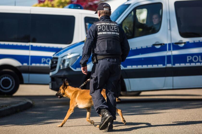 A police officer walks walks with a dog past police vehicles in a street in Rottenburg am Neckar, southern Germany, Friday, April 21, 2017 where a suspect was arrested in connection to the explosives attack on the team bus of Borussia Dortmund the week before. (Christoph Schmidt/dpa via AP)