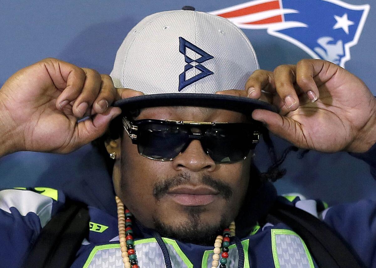 Seattle Seahawks running back Marshawn Lynch adjusts his cap -- made by an NFL licensee and in Seattle Seahawks colors -- during an "interview" Thursday in the run-up to Super Bowl XLIX.