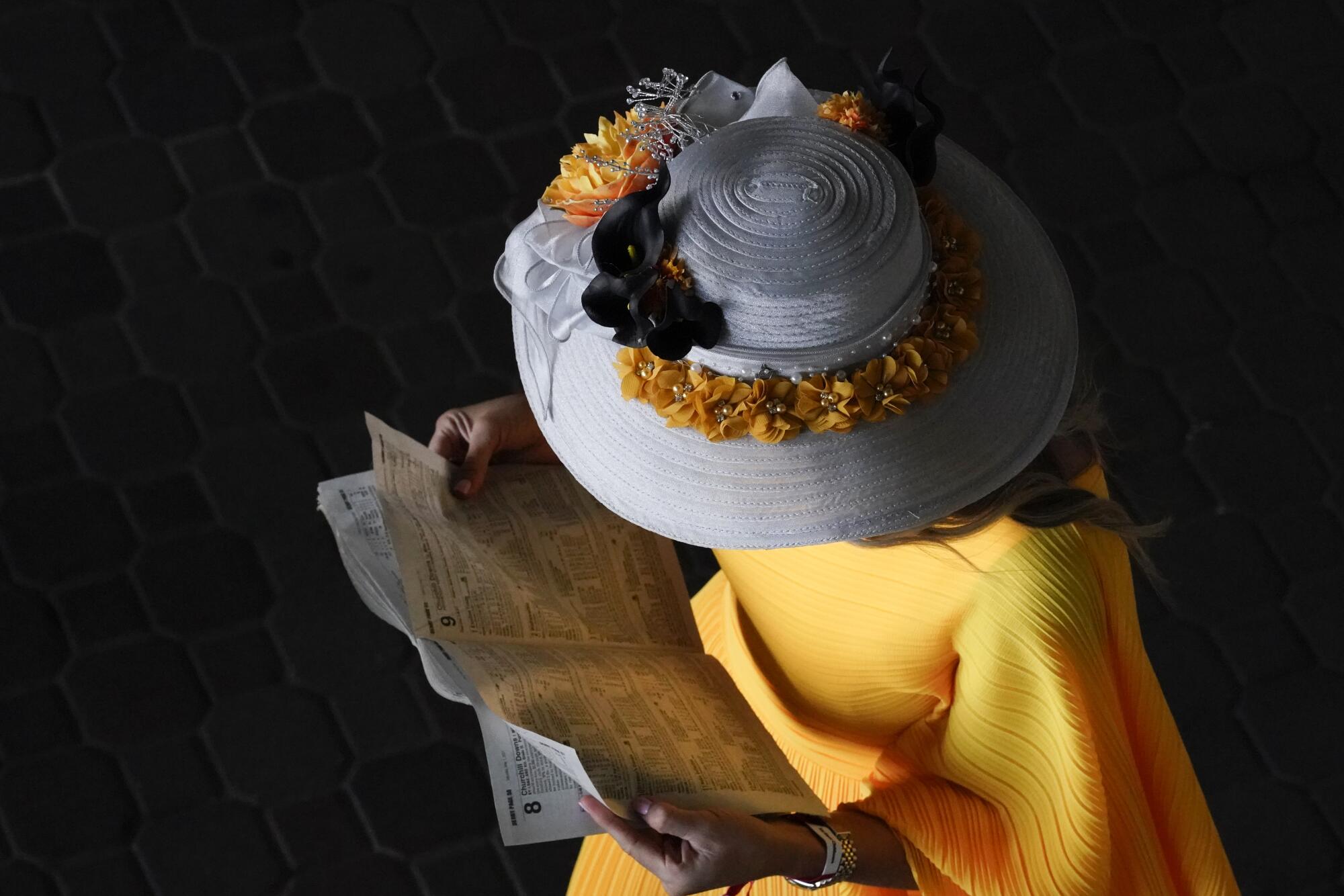 A woman wears a gray brimmed hat with yellow flowers around the brim and a yellow dress.