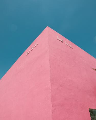 The corner of a pink building juts up into the blue sky. 