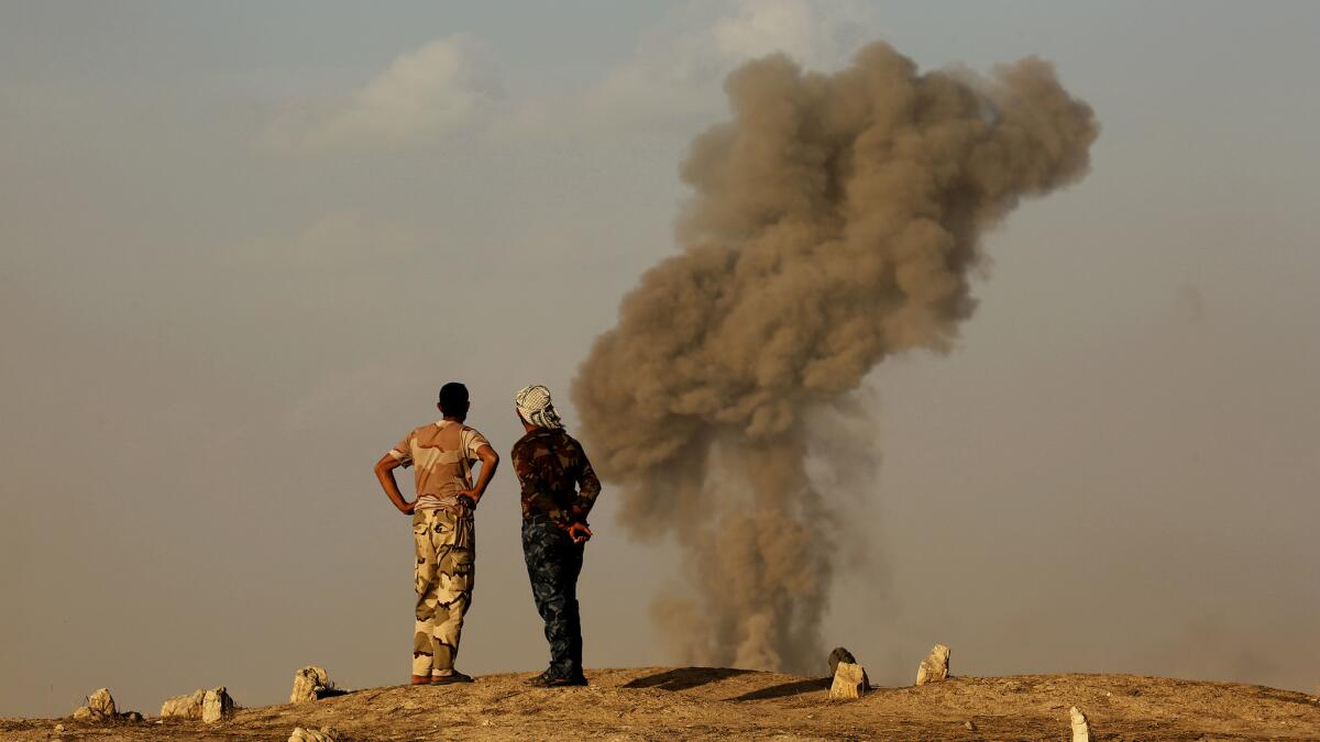 Members of Iraq’s popular mobilization units watch smoke rise from a bombing near Zarqa, Iraq.