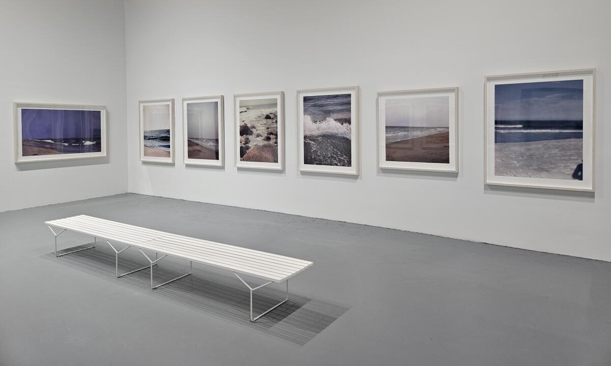 A white bench and seven landscape prints in a museum gallery