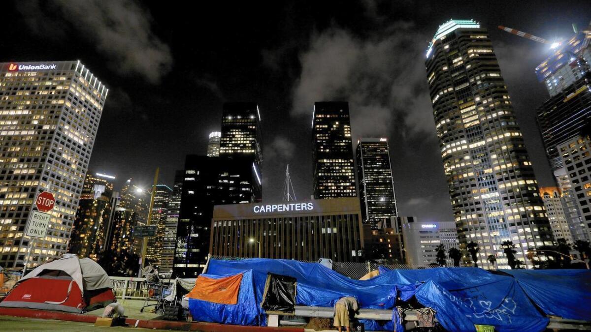 Una persona sin casa se prepara para dormir en un campamento callejero entre los sutiosos edificios del distrito financiero en el centro de Los Angeles.
