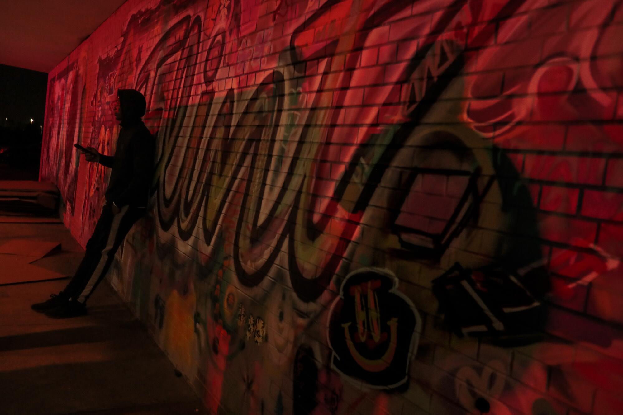 A student checks his phone as red and blue lights from a police vehicle reflect off a wall.
