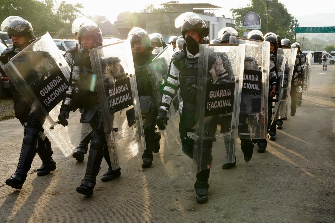 Uniformed people with helmets and shields walk in a group. 